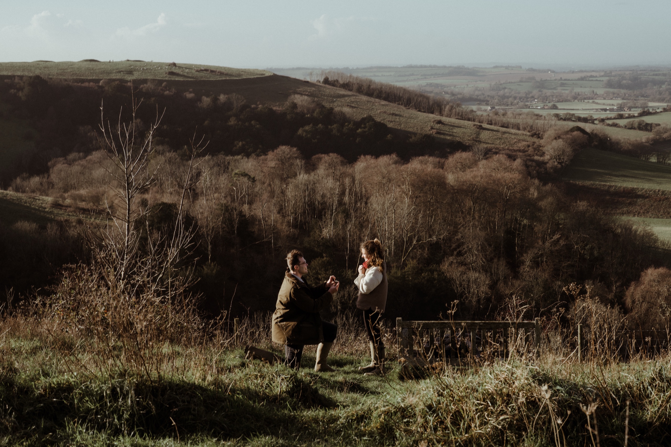 Vere on one knee, proposing to Ella on a hillside
